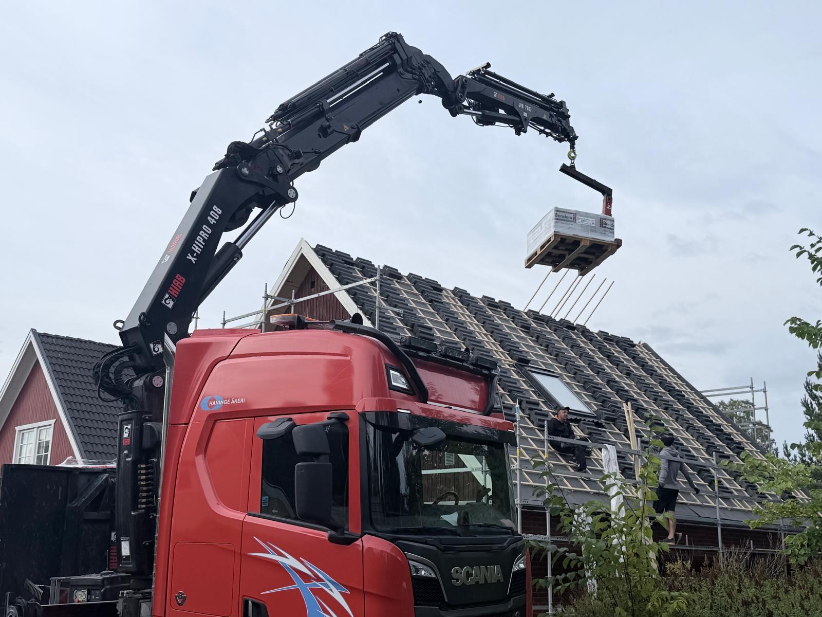 Pall med nya betongpannor lyfts upp till taket med kran